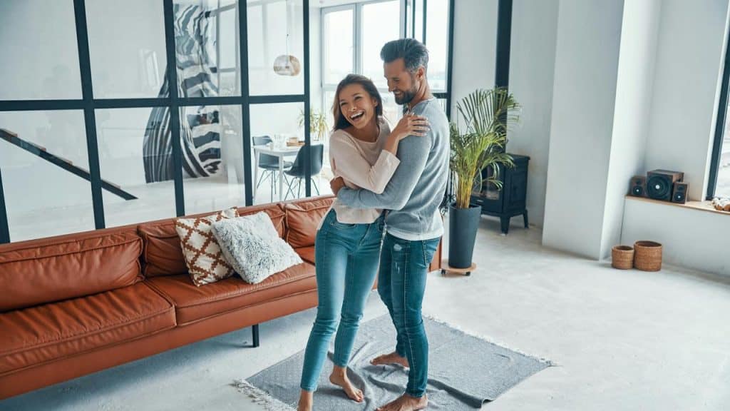 A couple laughs and dances together in a bright modern living room.