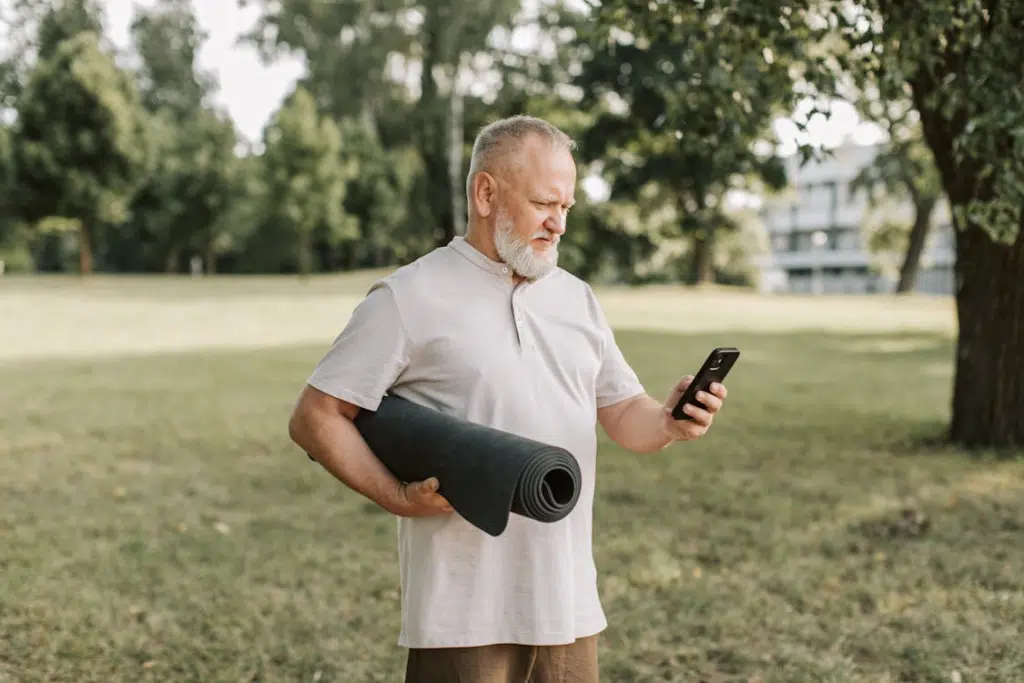 A man holding a yoga mat while using a phone