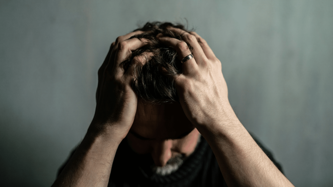 A man is grasping his head with both hands in distress, face turned down.