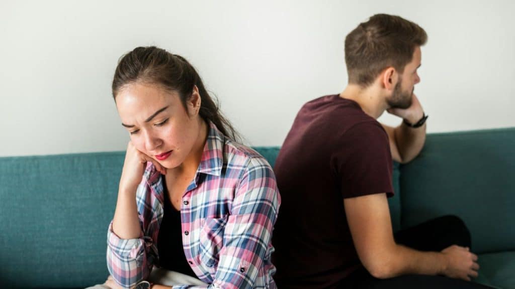 Disappointed woman in plaid shirt sitting on a couch, facing away from a man.
