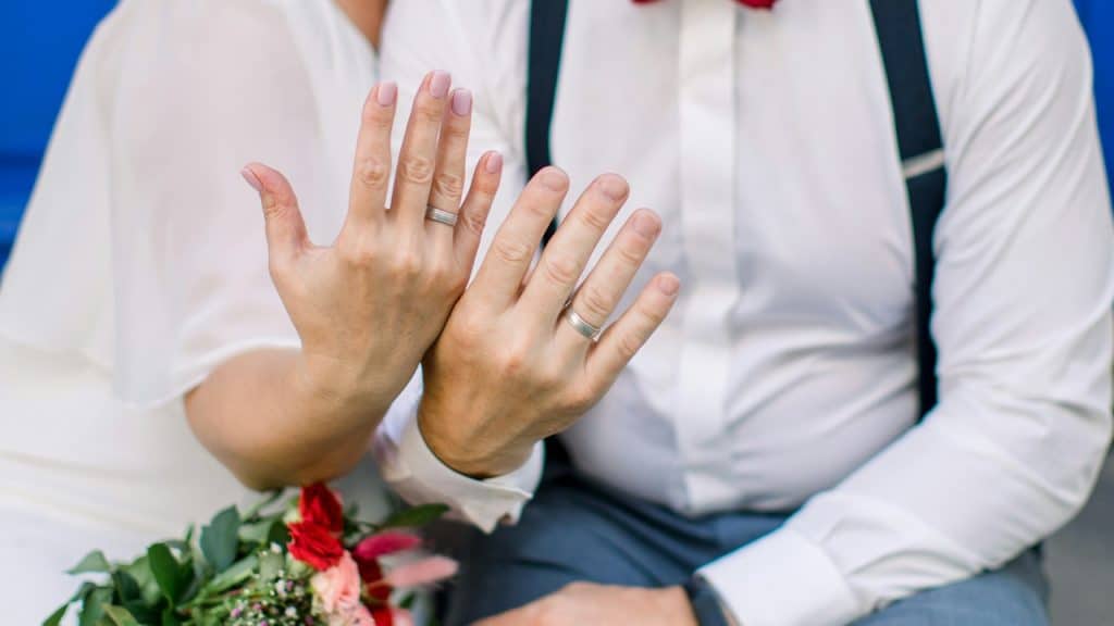A couple holding up their hands and showing off their wedding rings.