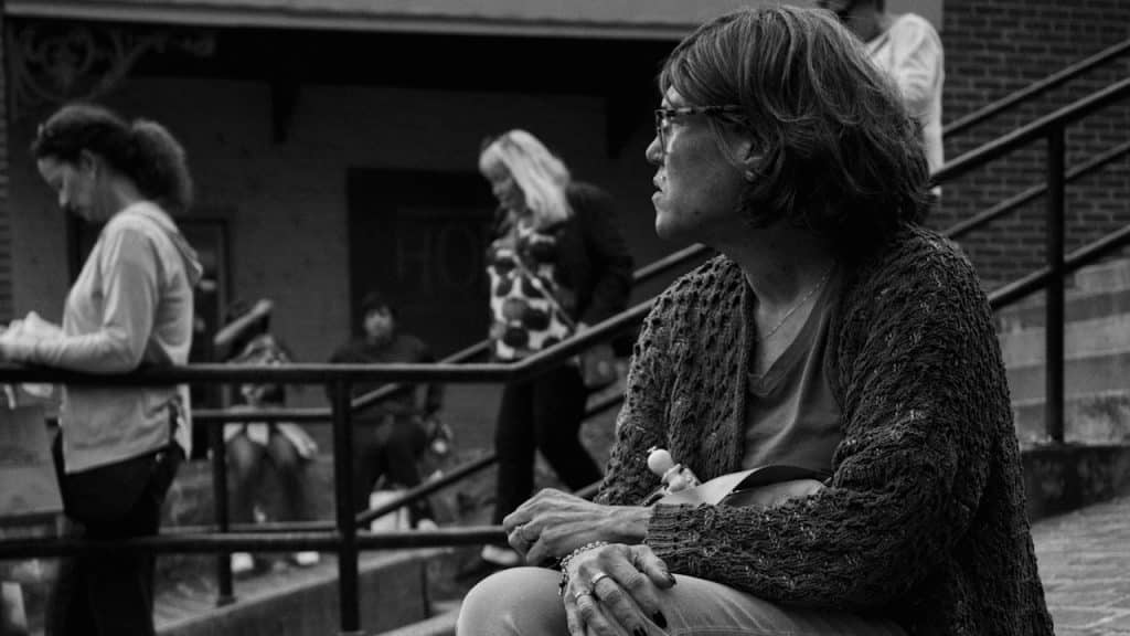 An older woman wearing glasses is sitting on stairs.