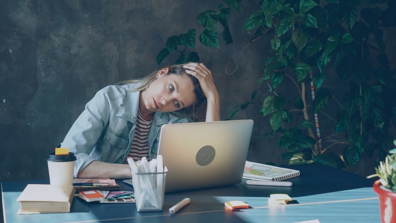 A woman appears stressed while working on a laptop.