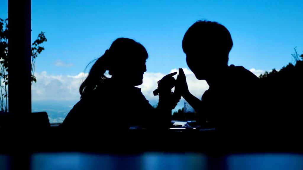A silhouette of a couple holding hands at a table with a blue sky in the background.