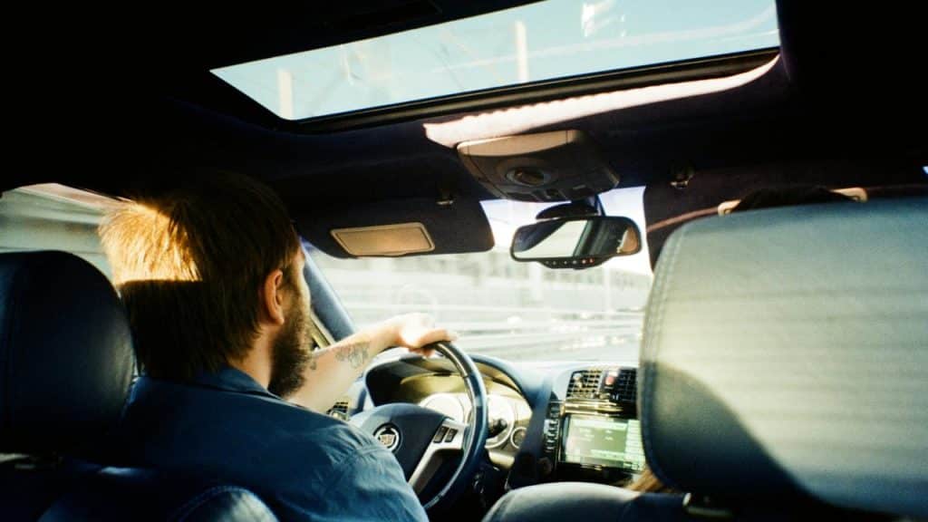 A man driving a car with sunlight streaming through the sunroof.