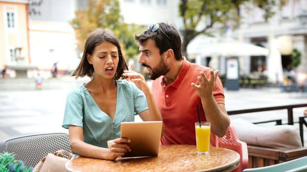 A distressed couple argues fiercely while sitting at an outdoor cafe table.