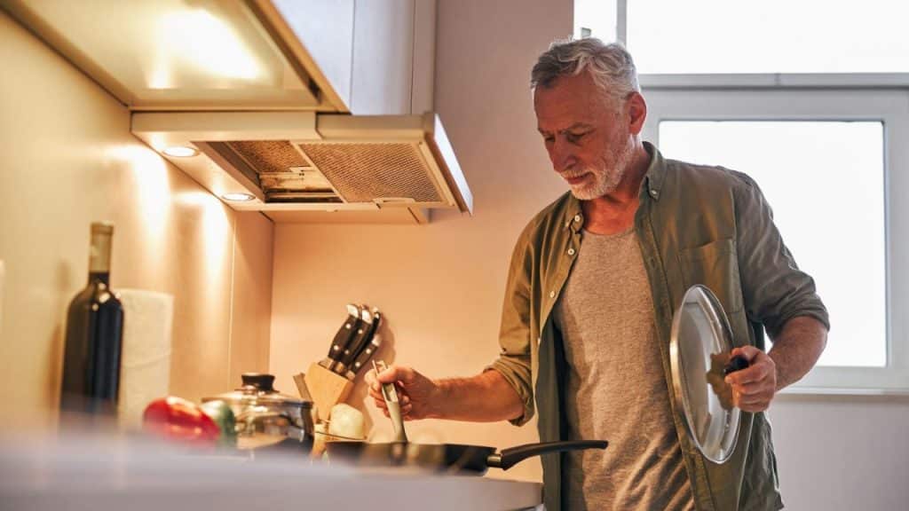 Middle-aged man cooking at a stove in a brightly lit kitchen.