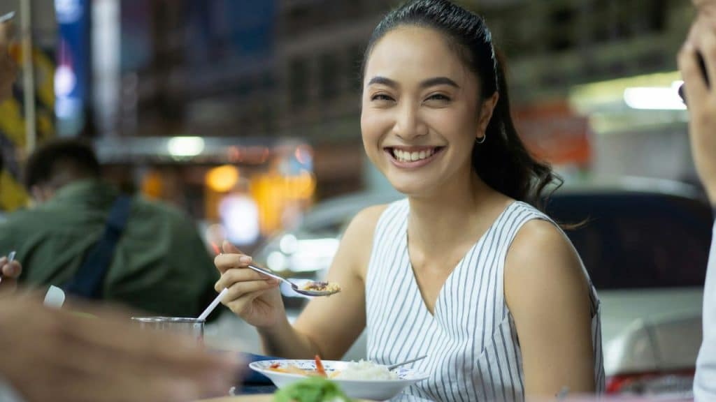 Young woman smiling brightly while eating food outdoors at night.