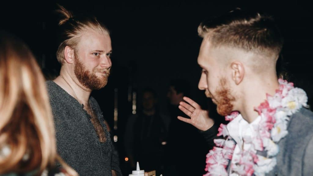 Two men with beards talking to each other at night, one wearing a flower lei.