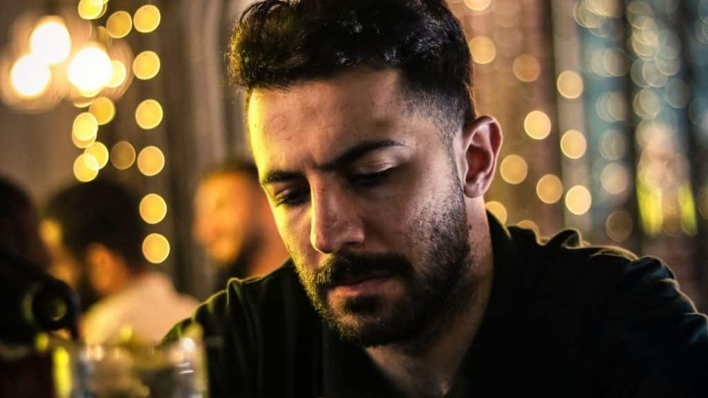 Close-up of a serious man with a beard looking down in a dimly lit setting.