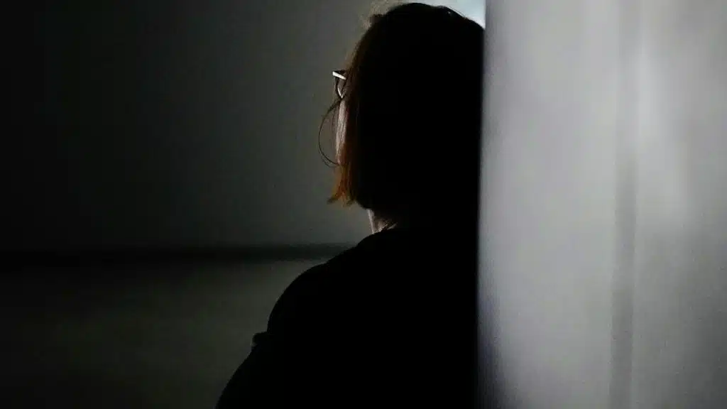 A woman leaning against a wall in dim light.