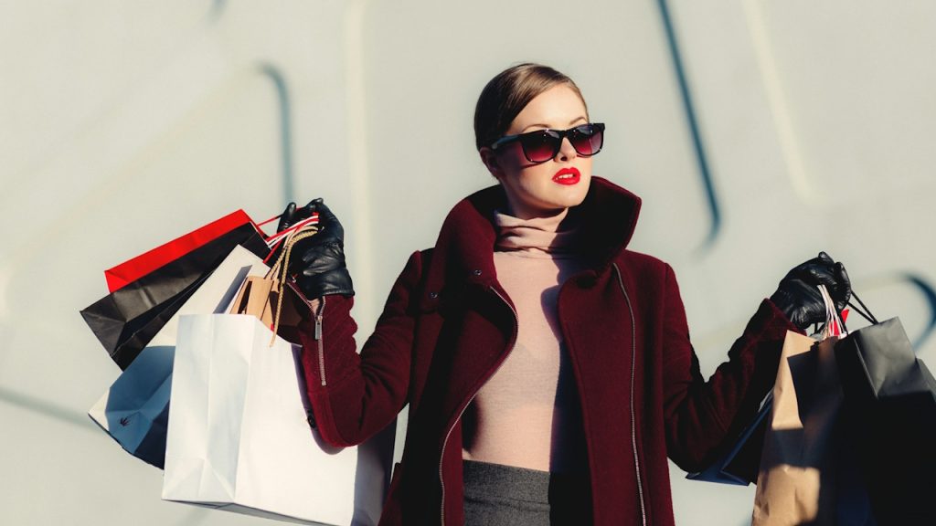 A woman holding shopping bags and wearing sunglasses.