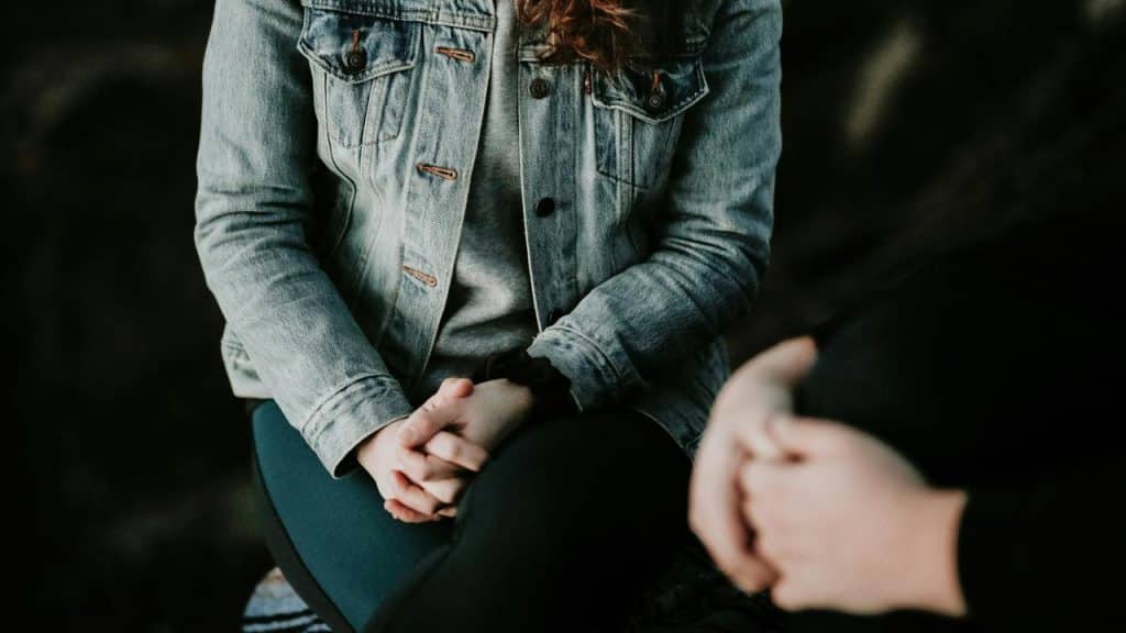 A close-up of two people sitting and talking with their hands clasped.