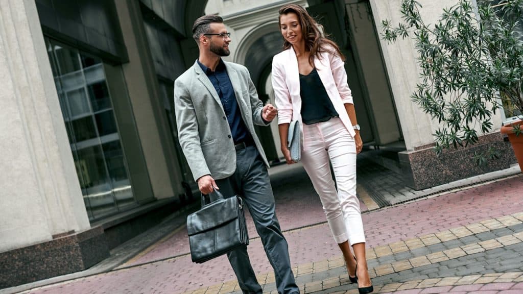 A professional looking couple walking across a street with the man holding a briefcase.
