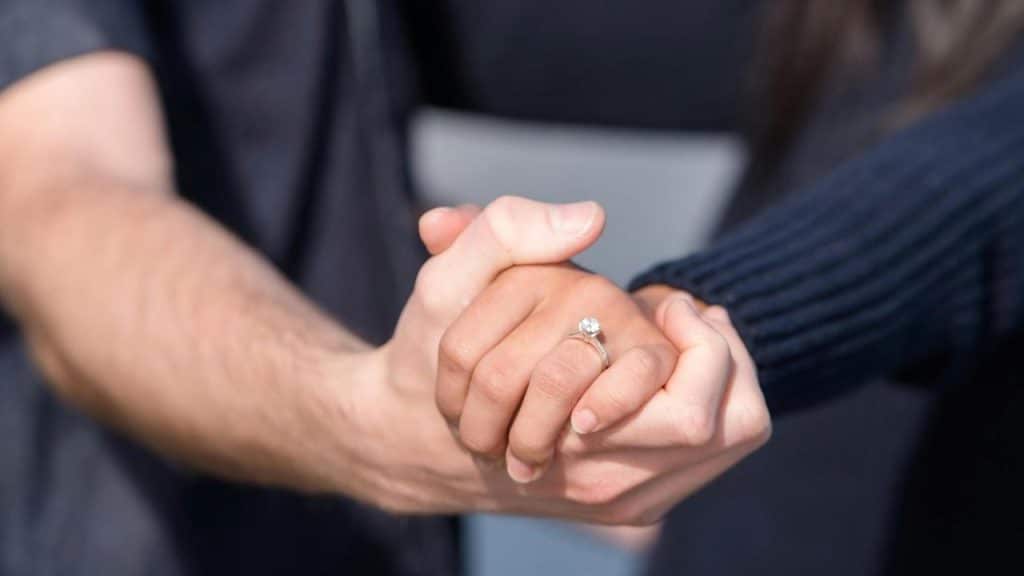 A close-up of a couple holding hands with an engagement ring visible.