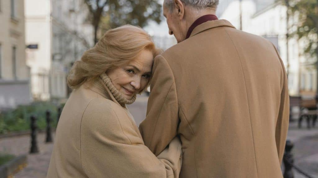 An elderly woman smiling while walking arm in arm with a man down a city street.