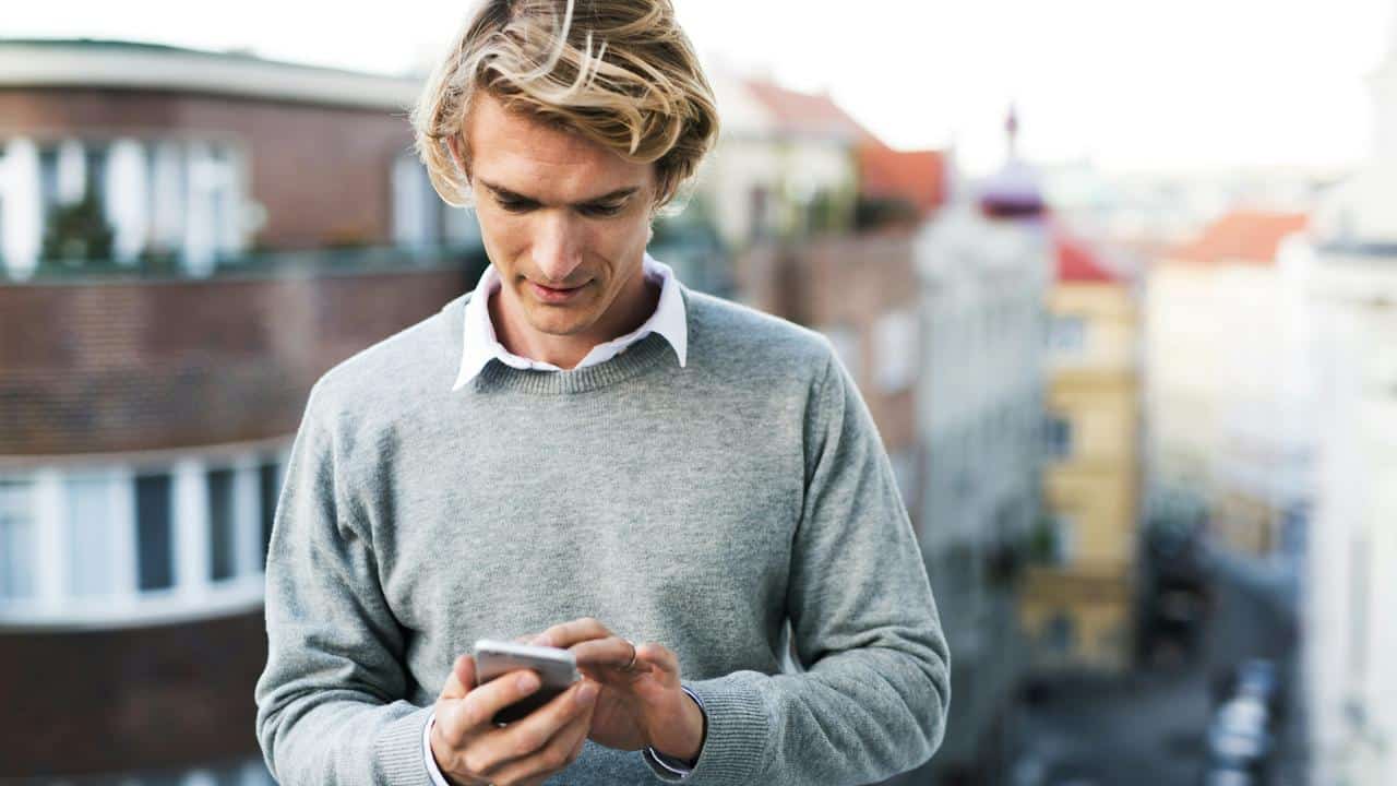 A man in a gray sweater looking at his phone outdoors.
