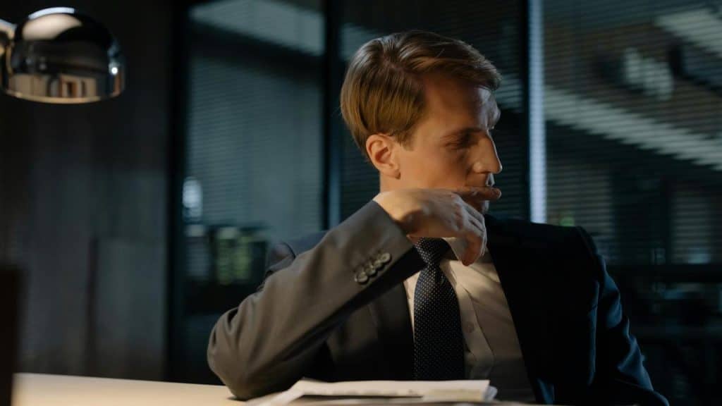 A man in a suit sitting at a desk, looking to the side.