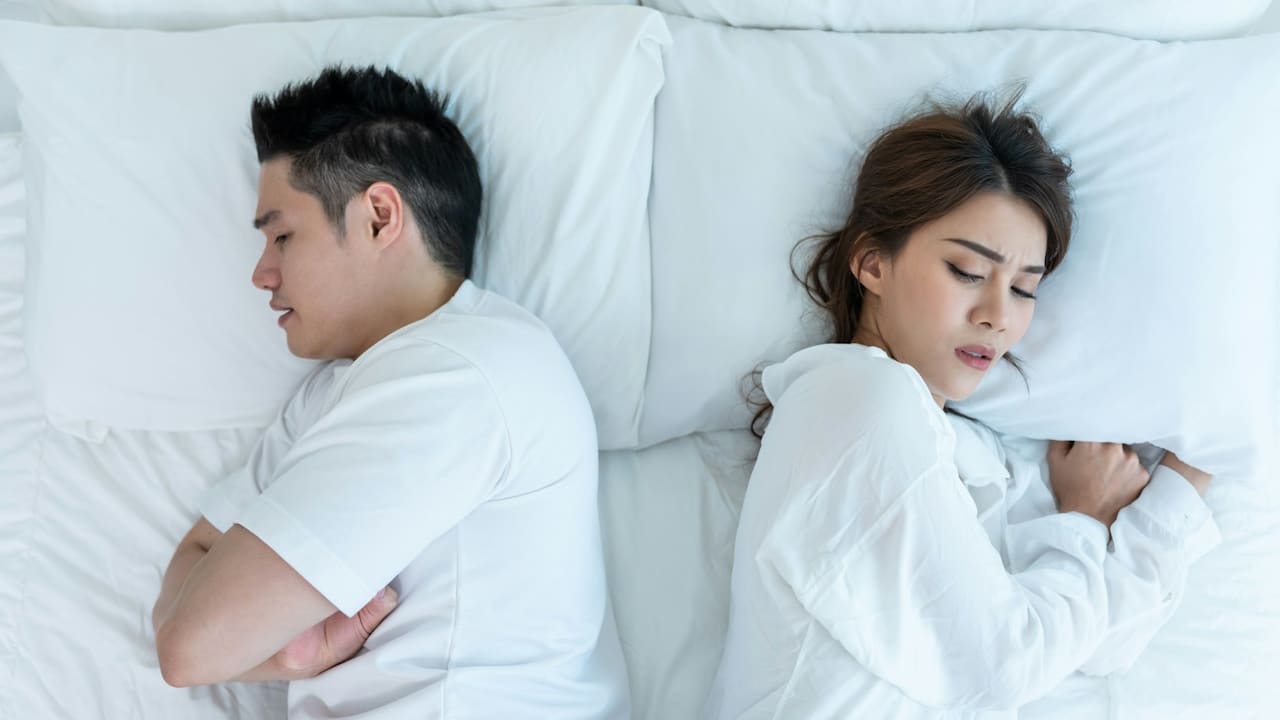 A young couple lying on a bed with painful expressions after a fight.