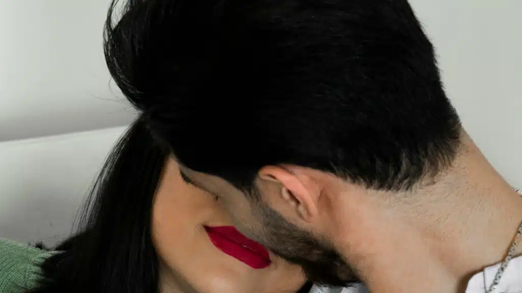 A man with his face hidden is kissing a woman with dark pink lipstick.