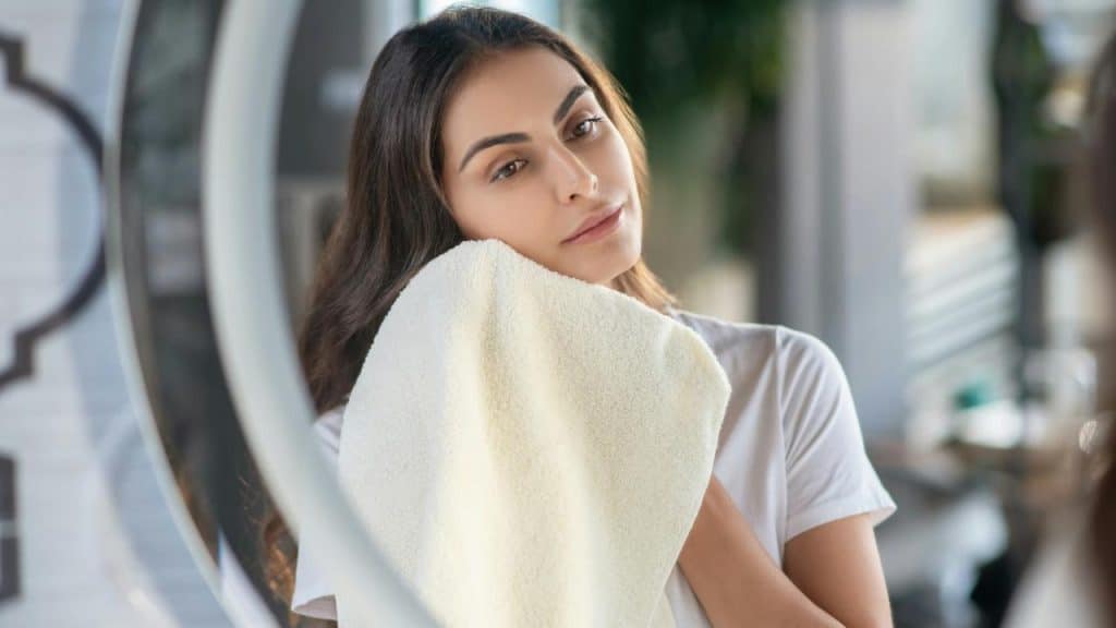 A woman drying her face with a towel in front of a mirror.