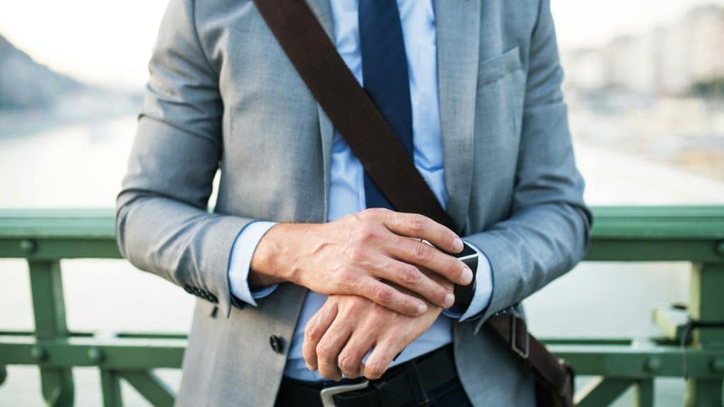 A man in a suit standing outdoors and checking his watch.