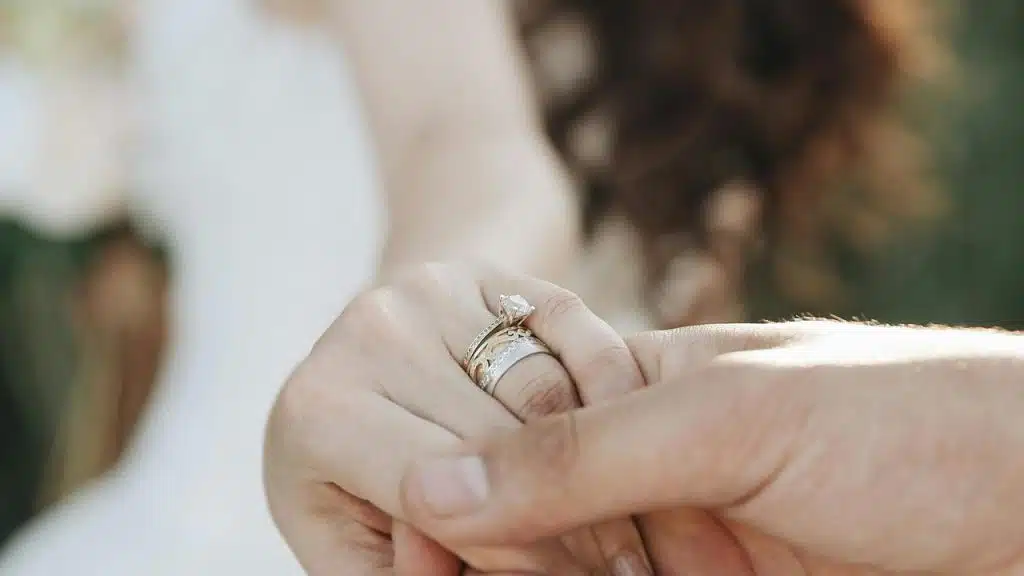 A close-up of a bride’s hand with a wedding ring being held by a groom’s hand.