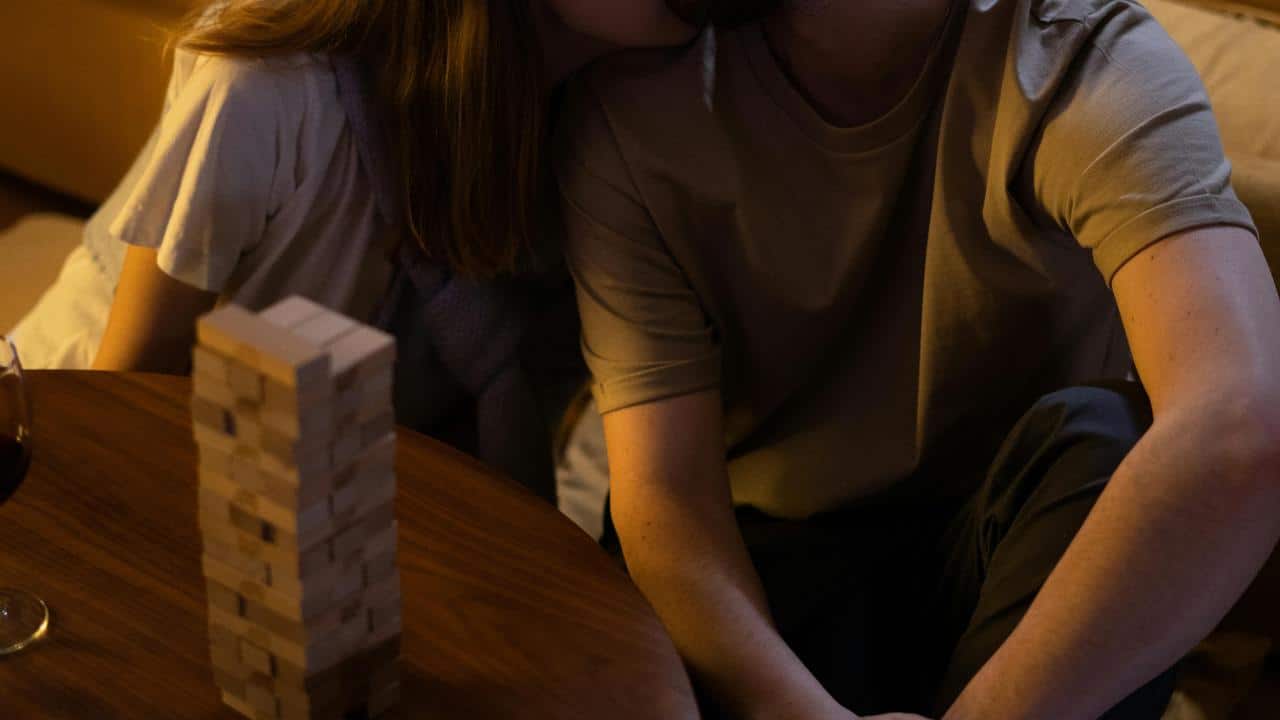 A couple sitting close together beside a Jenga tower on a table.