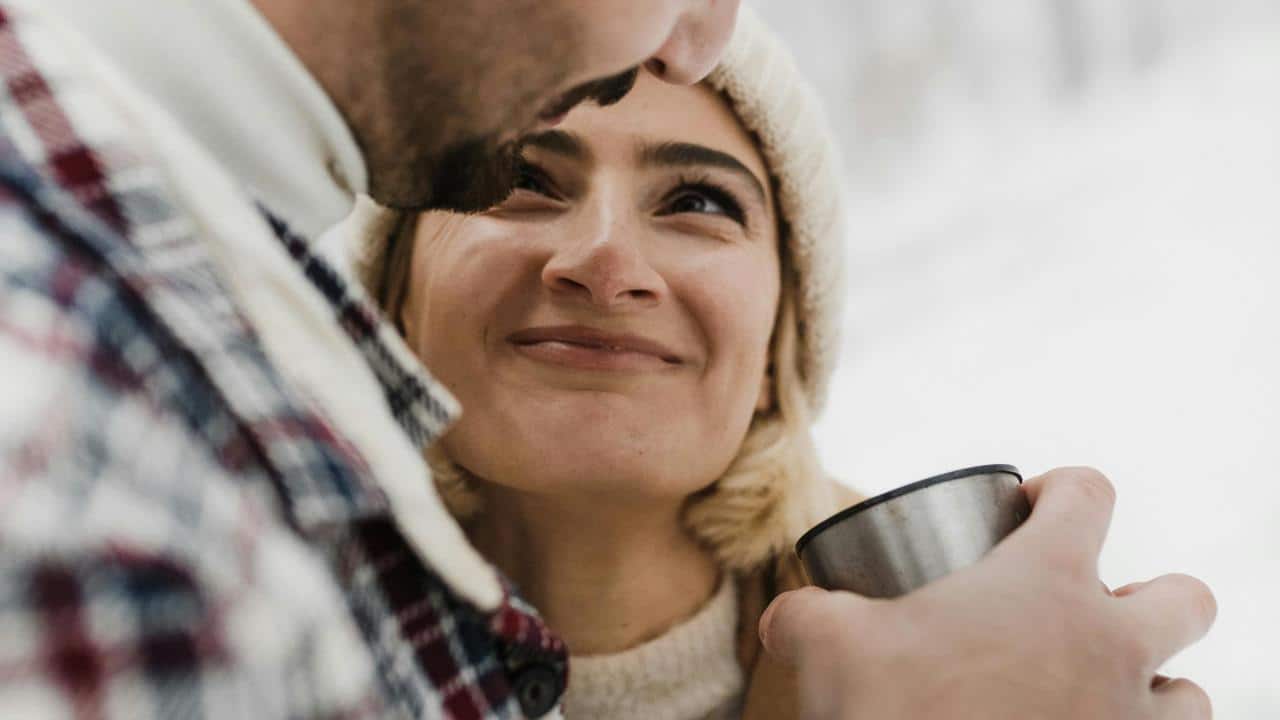 A woman smiling warmly at someone holding a metal cup in a snowy setting.