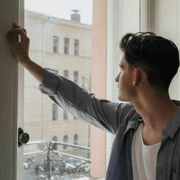 A man looking out a window while holding the frame.