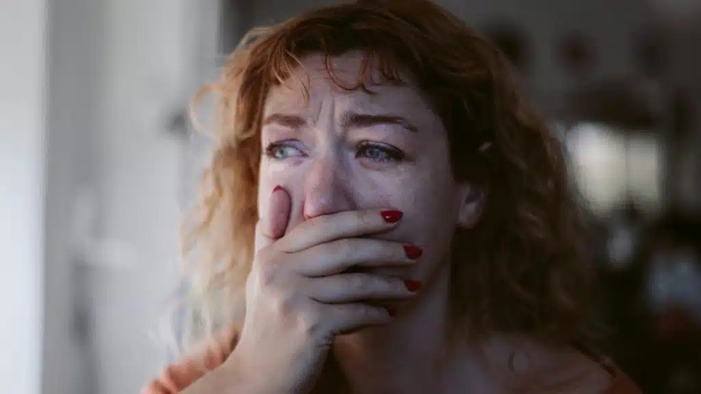 A woman with tearful eyes covers her mouth in distress.