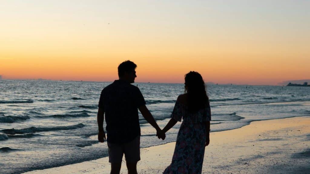 A couple holding hands while walking along the beach at sunset.