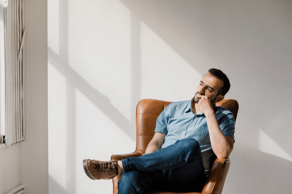 Man in Blue Crew Neck T-shirt and Blue Denim Jeans Sitting on Brown Leather Armchair