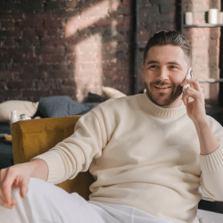 Bearded Man in White Knitted Sweater Sitting on Yellow Sofa Chair Using Cellphone