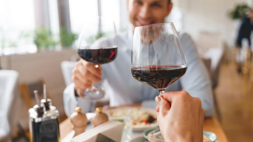 A close-up of two people clinking glasses of red wine at a restaurant.
