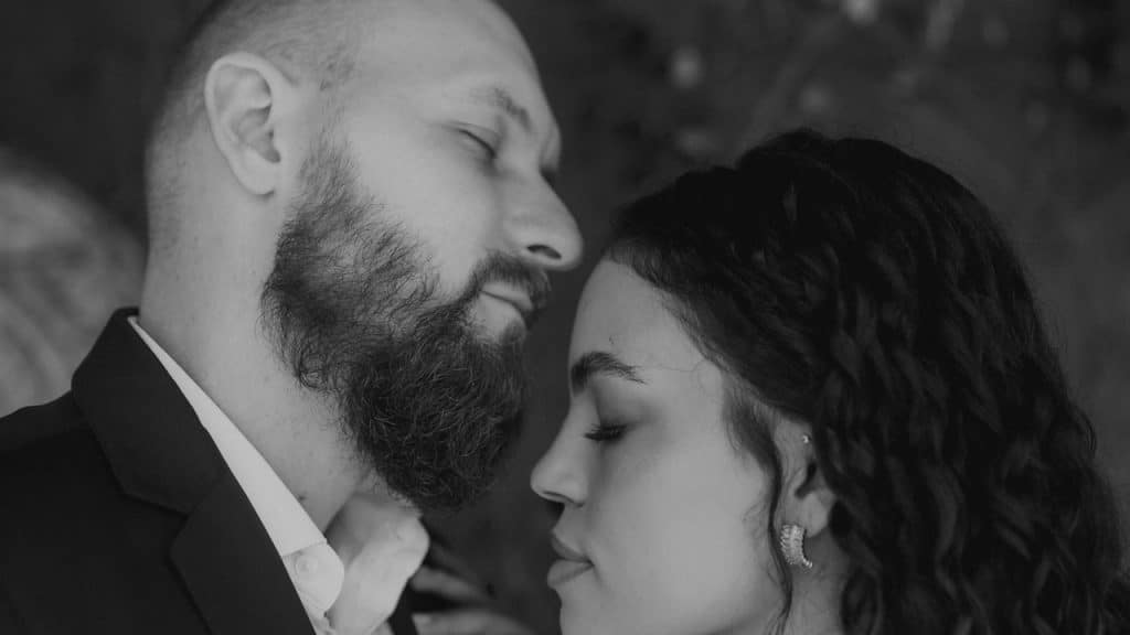 A bearded man is about to kiss a woman’s forehead.