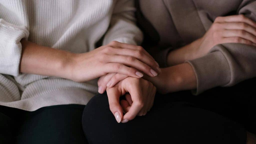 A close-up of one person gently holding another’s hand in a comforting gesture.