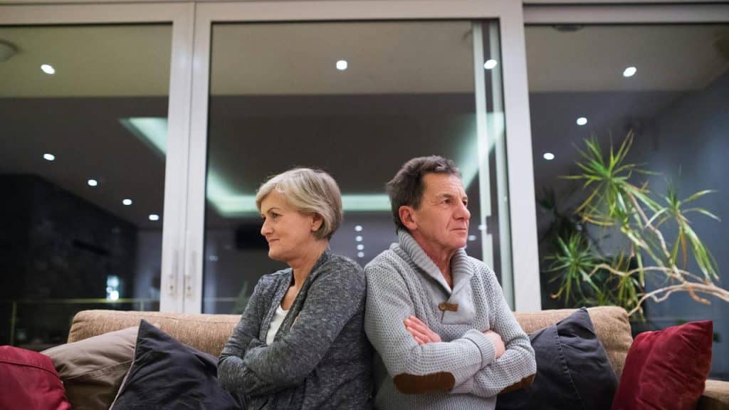 A middle-aged couple sitting back-to-back, looking upset.