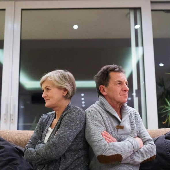 A middle-aged couple sitting back-to-back, looking upset.