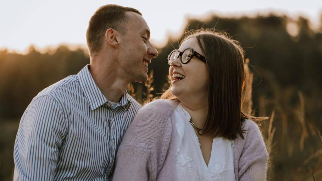 A couple smiling at each other on an outdoor grass field.