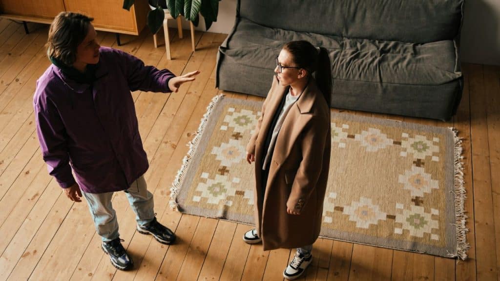 An overhead view of two people arguing in a living room, one in a purple jacket and one in a tan coat.