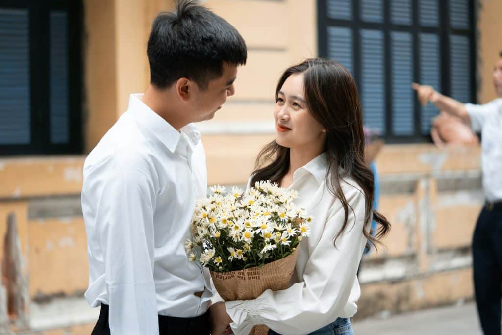 A man smiling at a smiling woman who is holding a bouquet of white flowers.
