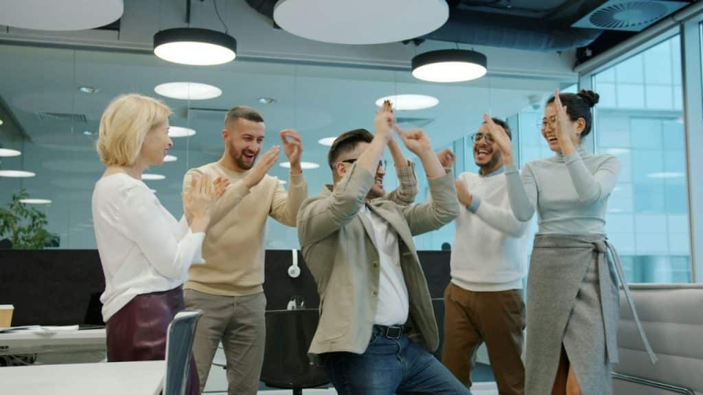 Five business colleagues cheering and high-fiving in a modern office.