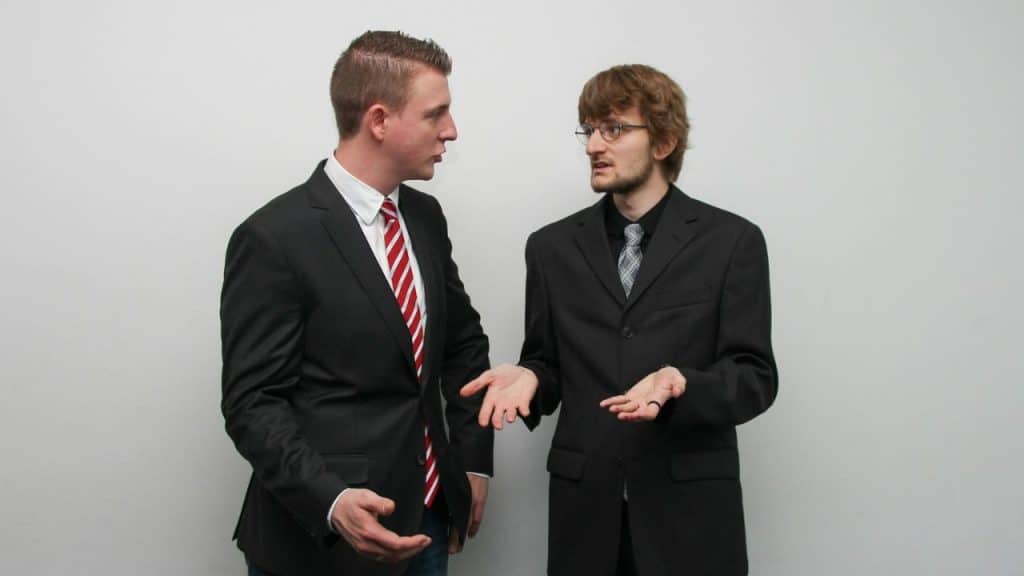 Two men in black suits and ties having an animated discussion with hand gestures.