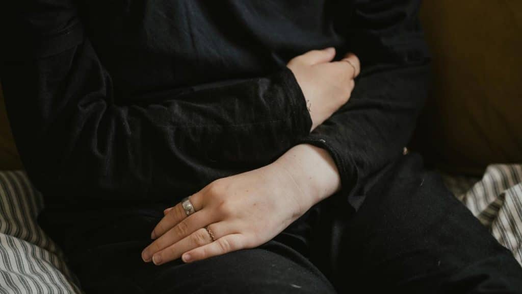 A person sitting with arms crossed over their stomach.