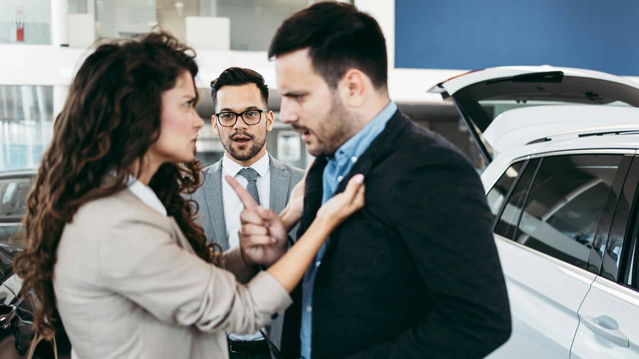 A woman argues with a man in a showroom while a salesperson watches them.