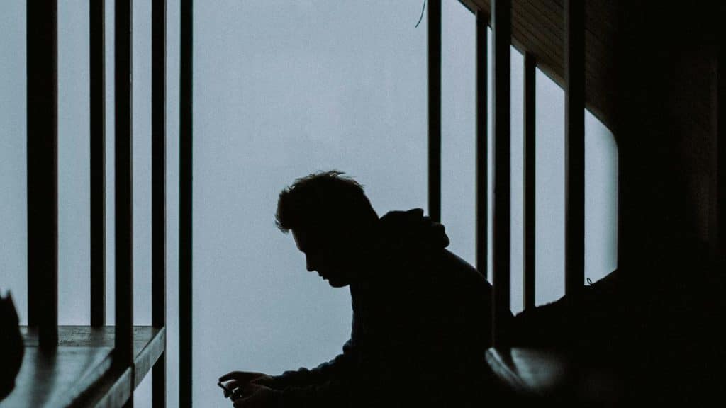A silhouette of a person sitting by large windows.