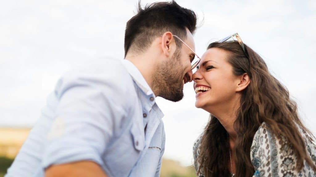 A laughing couple leans in close, smiling with their noses touching.