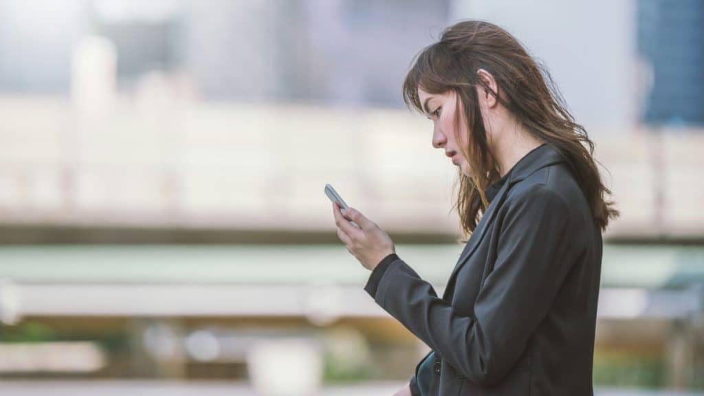 Woman in a business jacket looking intently at her cell phone outdoors in profile.
