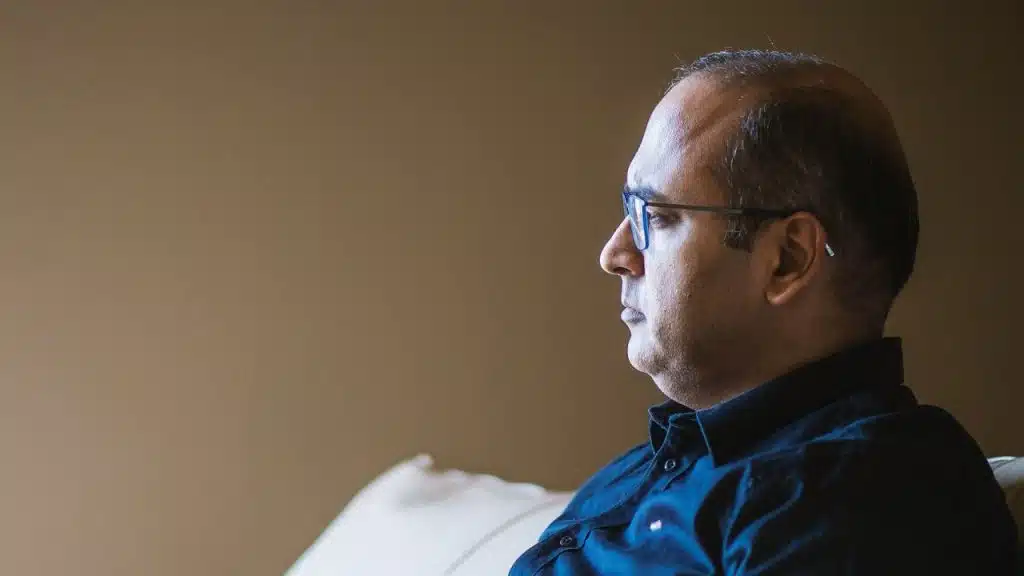 Profile view of a middle-aged man with glasses and a dark shirt looking off-camera.
